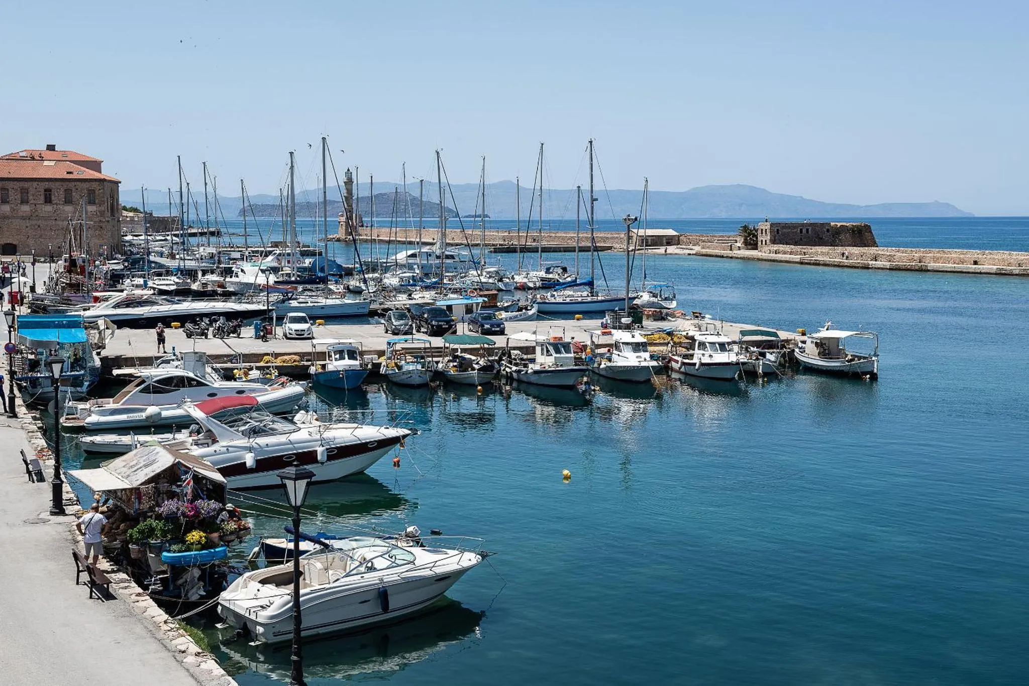Port de plaisance ensoleillé avec de nombreux bateaux amarrés et une promenade en bord de mer.