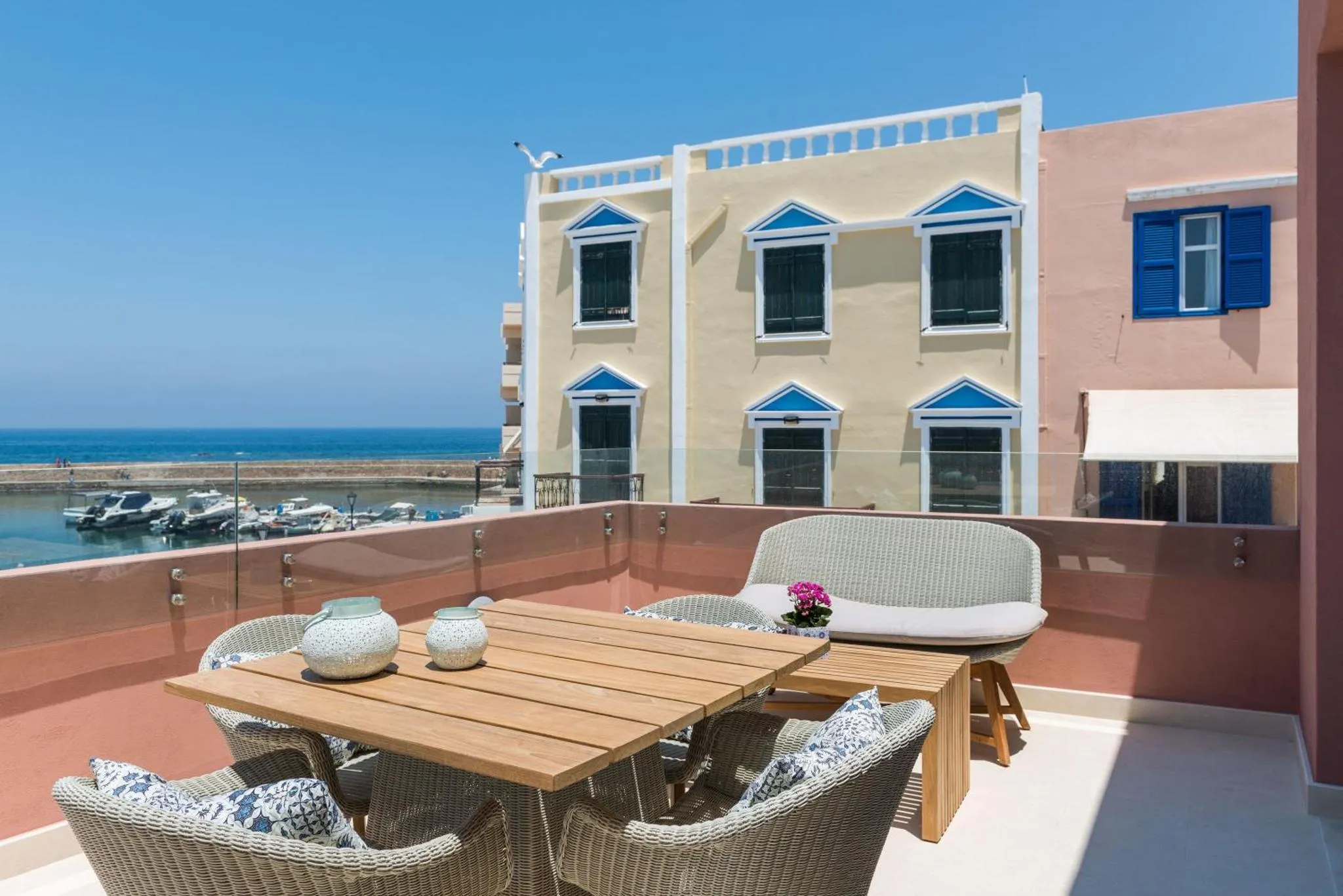 Terrasse aménagée avec table et fauteuils en osier, vue sur la mer et le port.