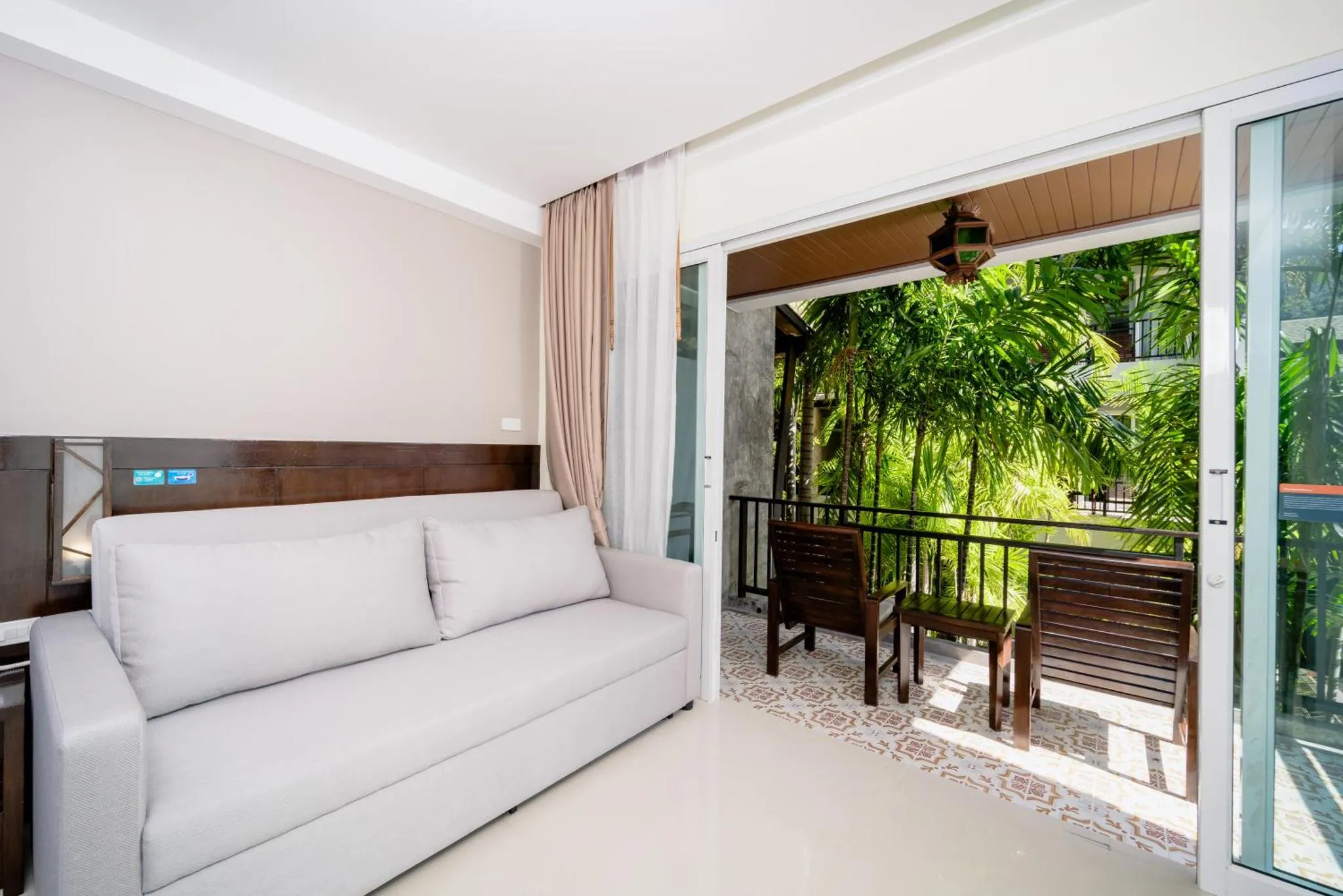 Espace de détente intérieur avec canapé blanc et accès à une terrasse ombragée.