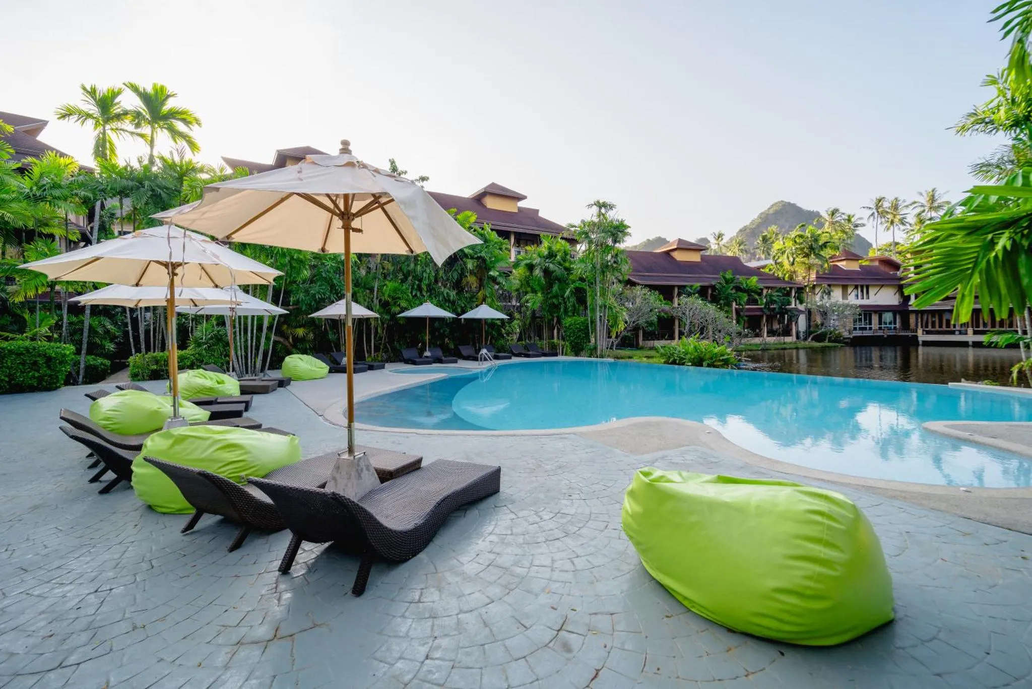 Transats et parasols bordent une piscine turquoise dans un jardin tropical.