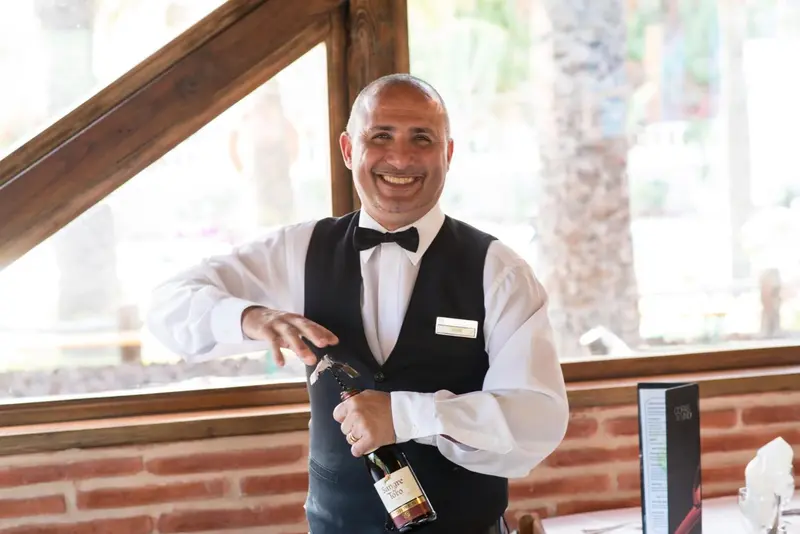 Un serveur souriant présente une bouteille de vin dans un restaurant.