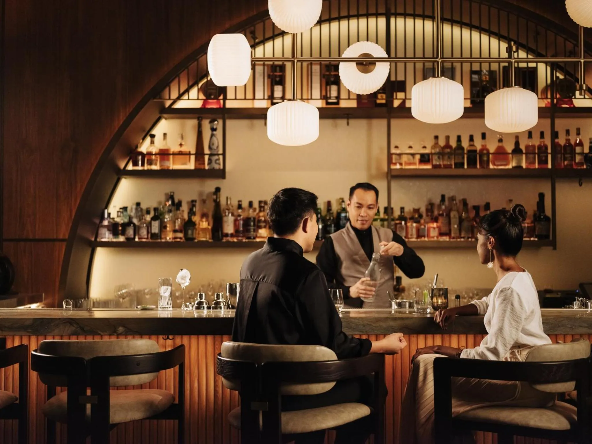 Un barman prépare une boisson pour des clients assis au comptoir.