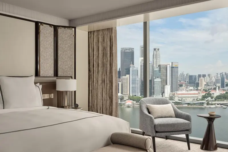 Une chambre avec un grand lit et un fauteuil près d'une fenêtre offrant une vue sur la ville.