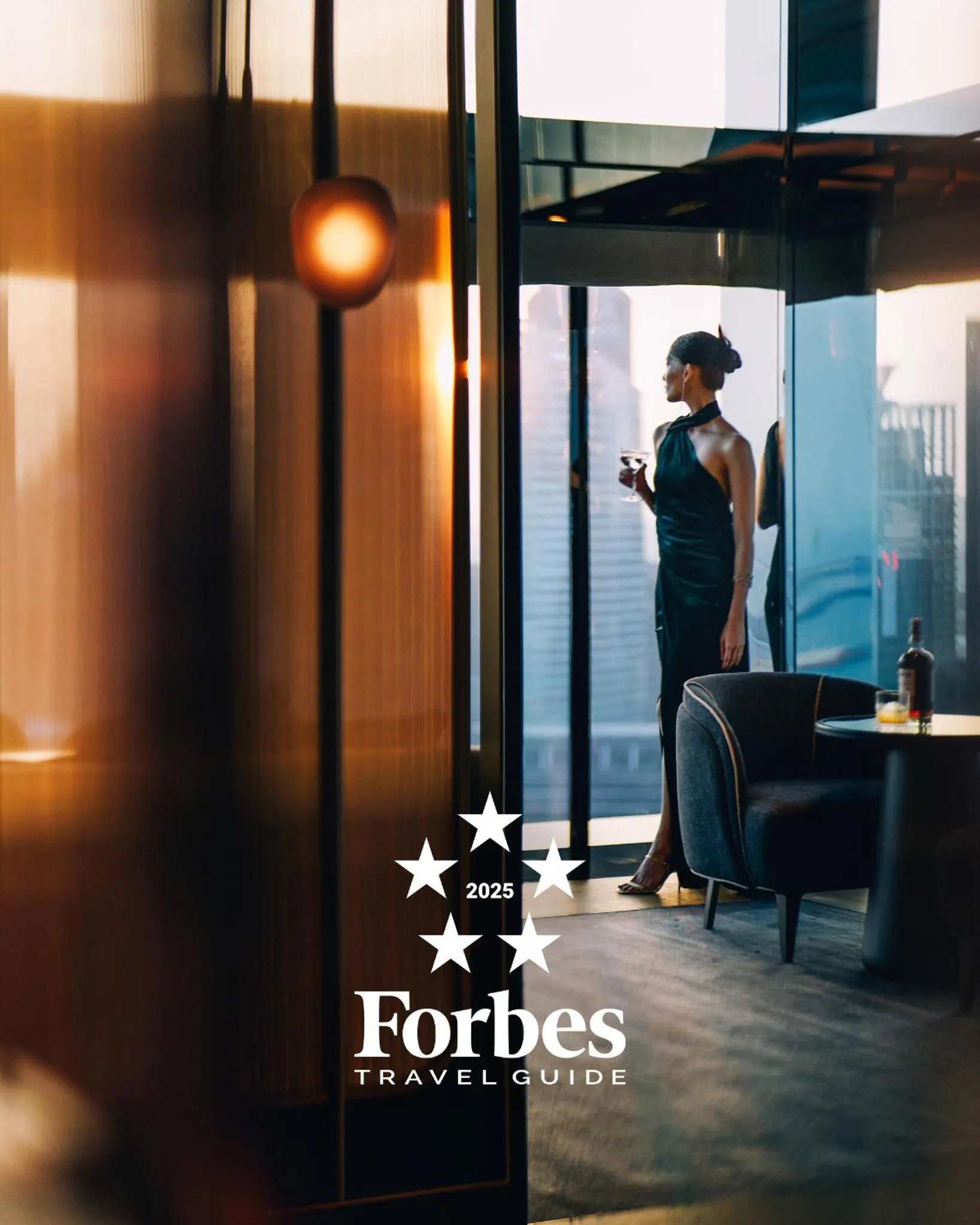 Une femme en robe noire déguste une boisson sur une terrasse avec vue sur la mer.