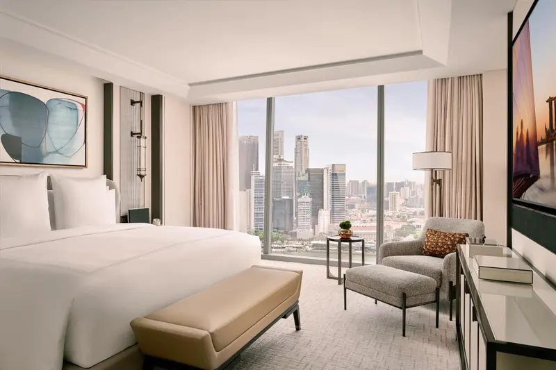 Chambre lumineuse avec un grand lit et une vue sur la ville.