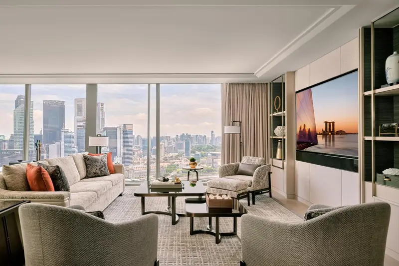 Un salon moderne avec canapés et fauteuils face à une grande fenêtre offrant une vue sur la ville.