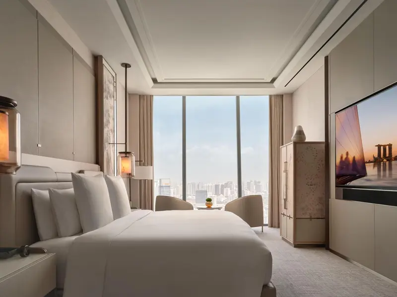 Chambre lumineuse avec un grand lit et une vue sur la ville.