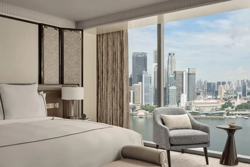 Une chambre avec un grand lit et un fauteuil face à une vue urbaine.