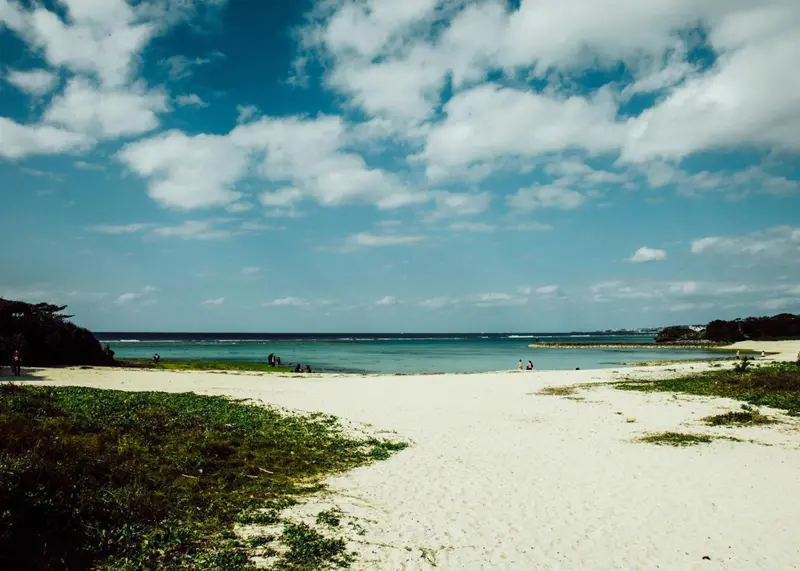 Plage de sable blanc bordée d'une végétation luxuriante sous un ciel nuageux.