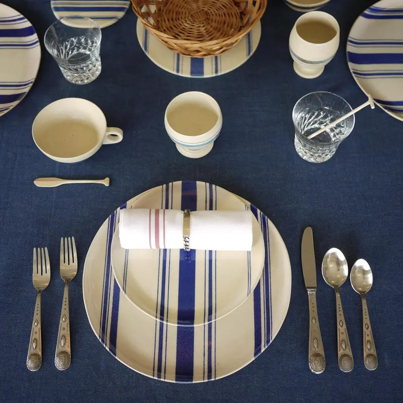 Une table est dressée avec de la vaisselle rayée et des couverts.