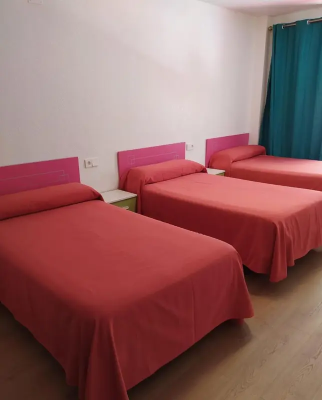 Trois lits simples dans une chambre aux murs roses et rideaux turquoise.
