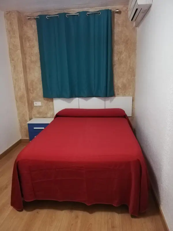 Une chambre avec un lit rouge et un rideau bleu.