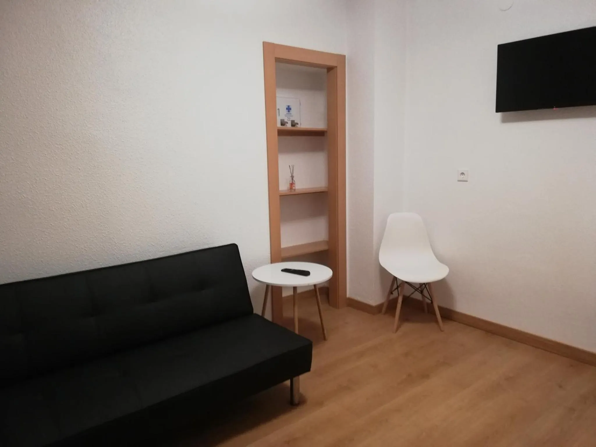 Une pièce lumineuse avec un canapé noir, une chaise blanche et une étagère en bois.