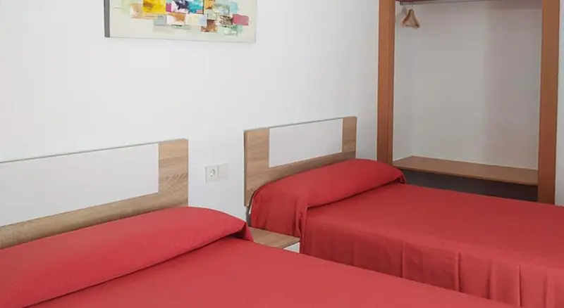 Deux lits simples avec des couvertures rouges dans une chambre lumineuse.
