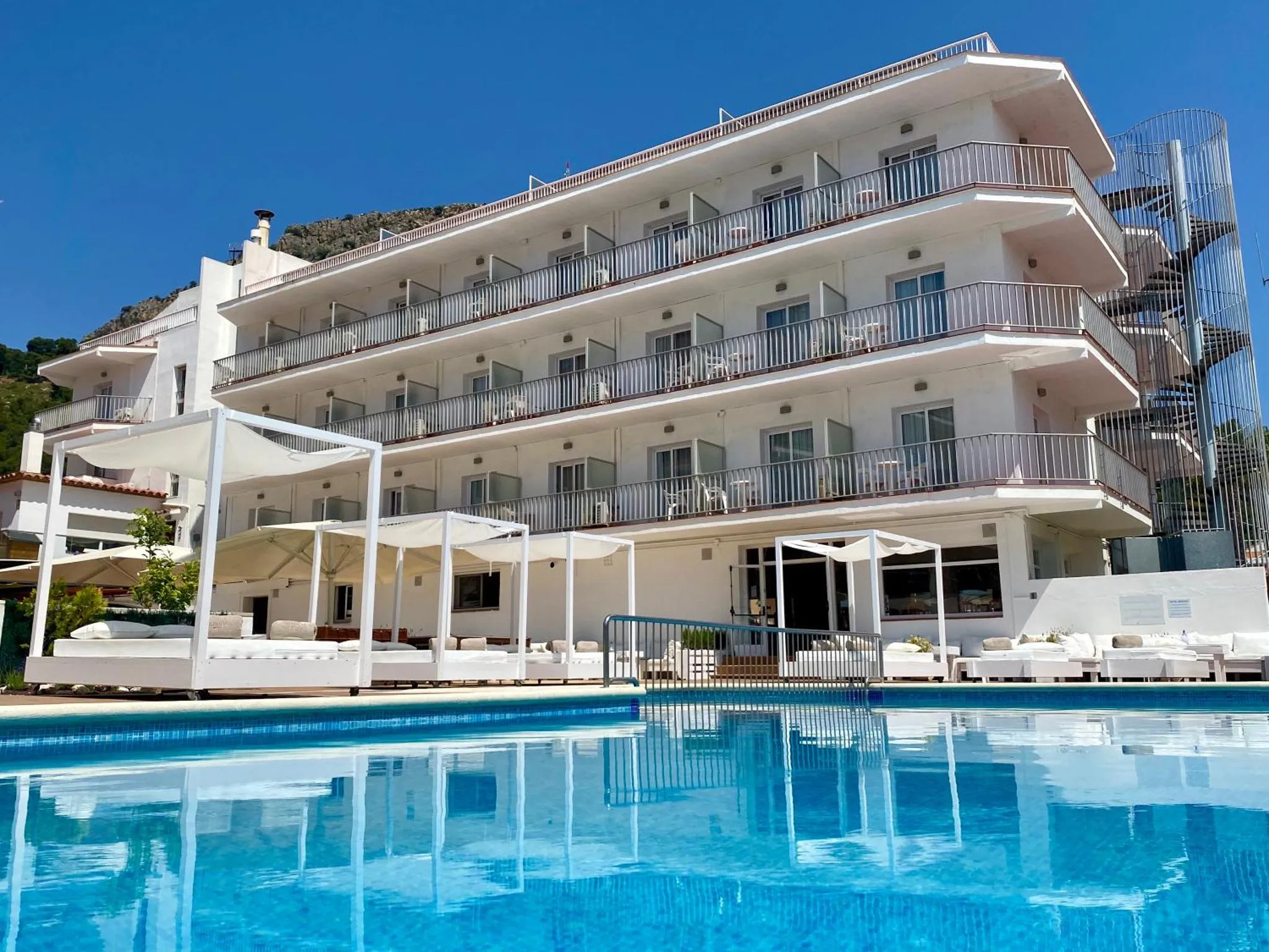 Bâtiment blanc à plusieurs étages avec des balcons surplombant une piscine bleu clair.