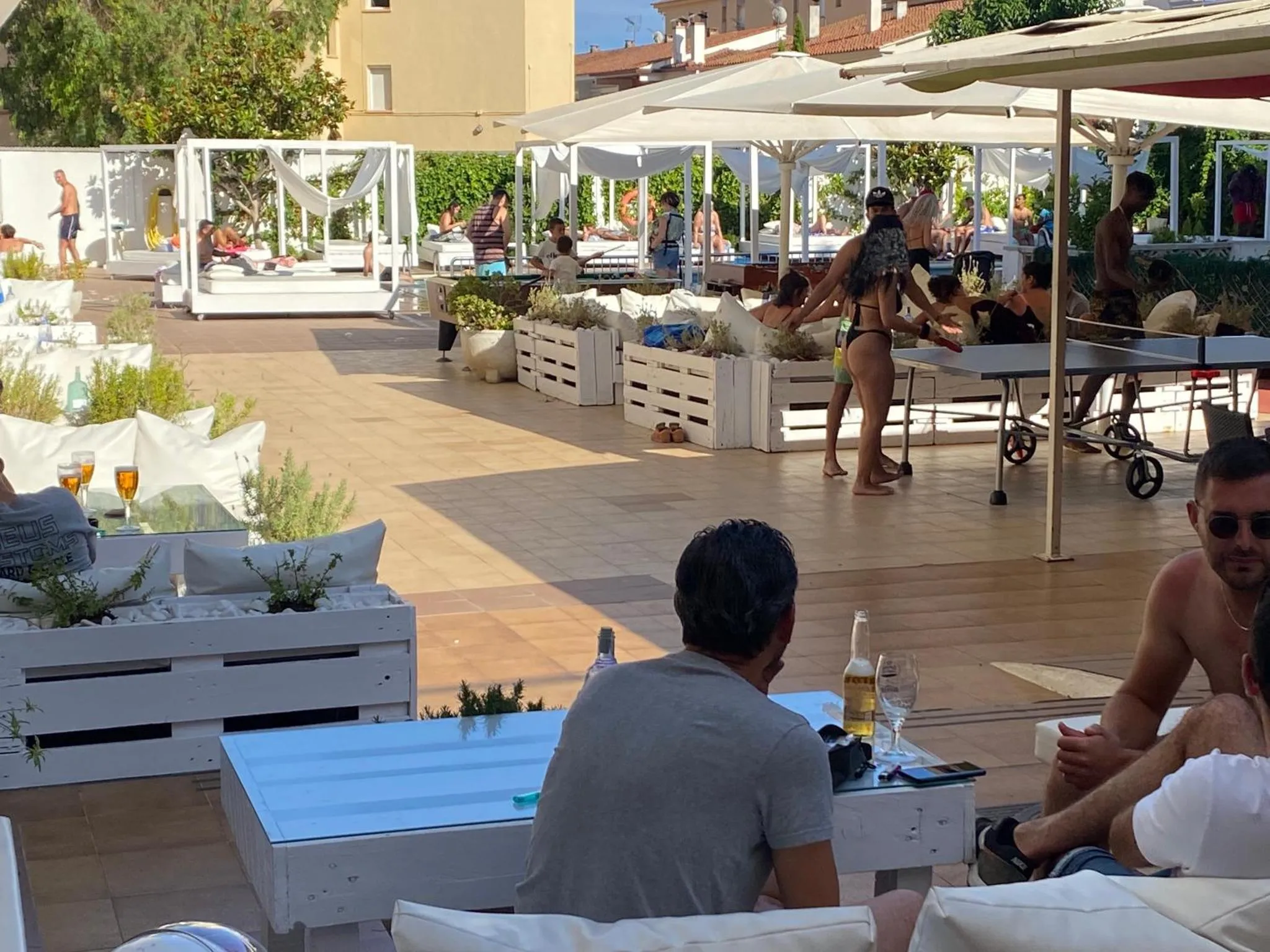 Terrasse ensoleillée avec des transats blancs et des clients assis autour de tables.