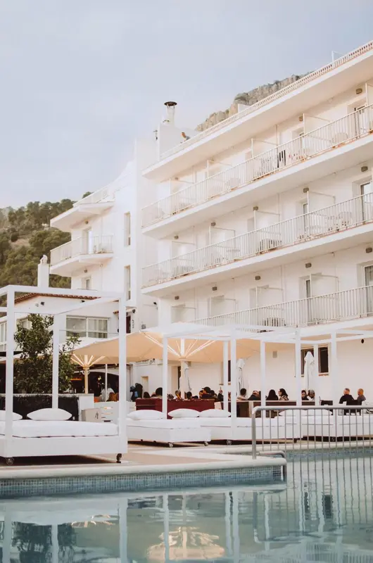 Bâtiment blanc à plusieurs étages avec des balcons et une piscine au premier plan.