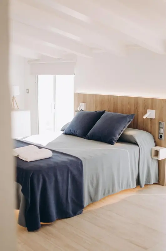 Une chambre lumineuse avec un grand lit recouvert d'une couverture bleue et de coussins.