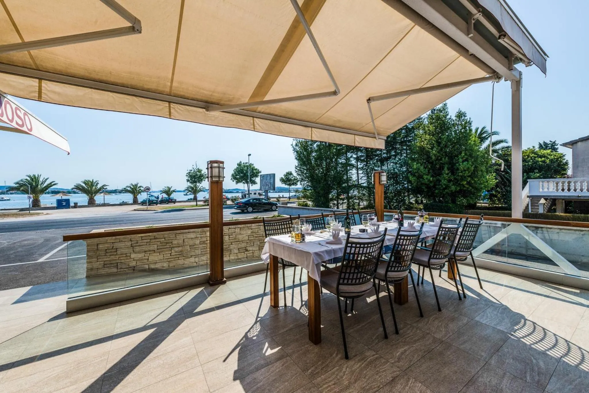 Une table est dressée sur une terrasse ombragée avec vue sur la mer.