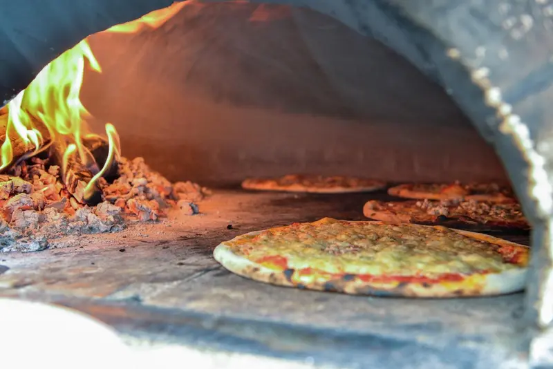 Des pizzas cuisent dans un four à bois.
