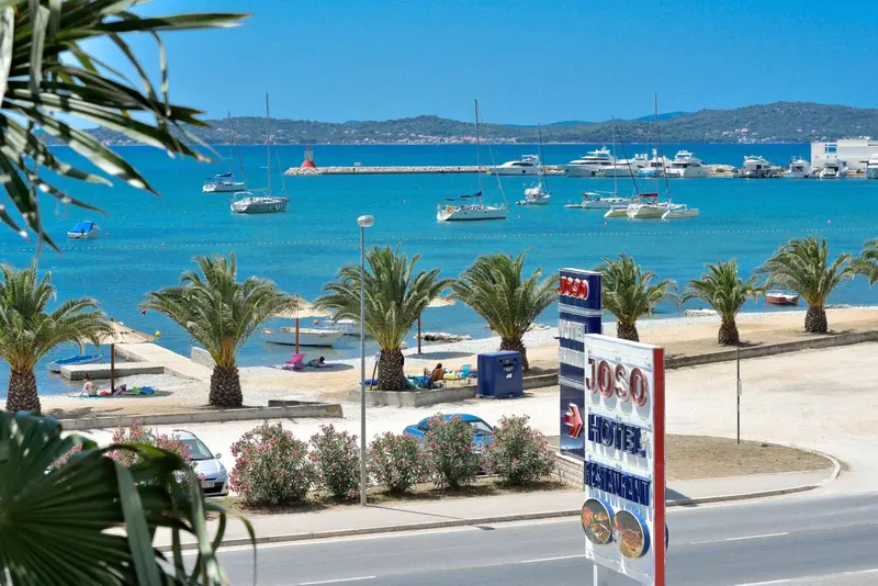 Vue sur une plage ensoleillée avec des palmiers et des bateaux amarrés dans un port.