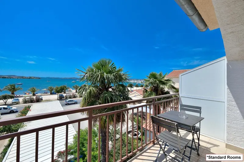 Une terrasse avec une table et des chaises offre une vue sur la mer et la végétation.