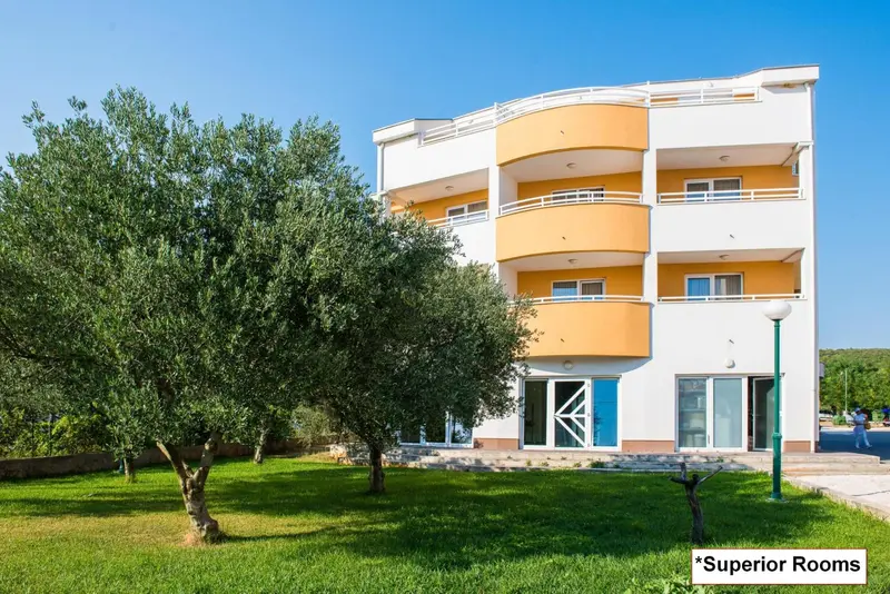 Bâtiment à étages avec des balcons et une végétation luxuriante devant.