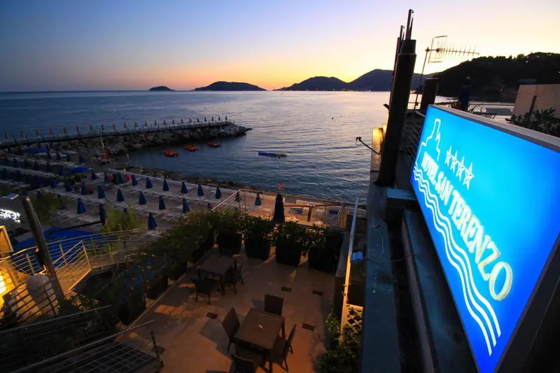 Terrasse avec tables et chaises donnant sur la mer au coucher du soleil.