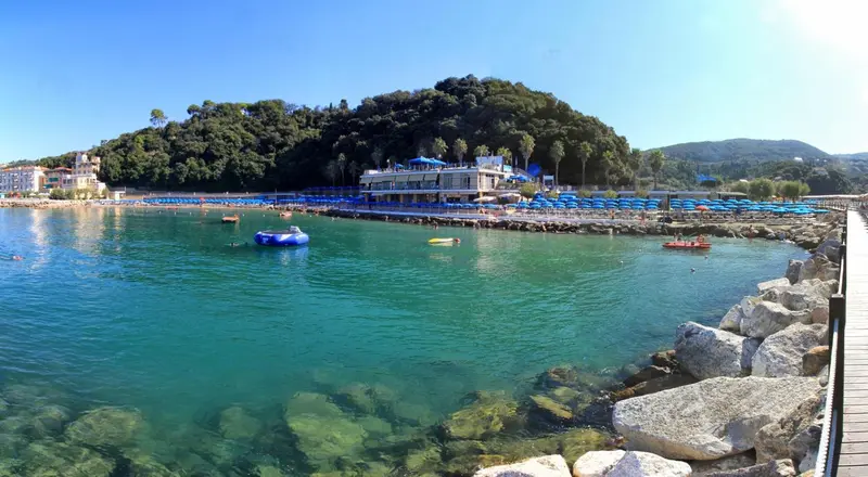 Une plage ensoleillée bordée d'une eau turquoise et d'une promenade rocheuse.