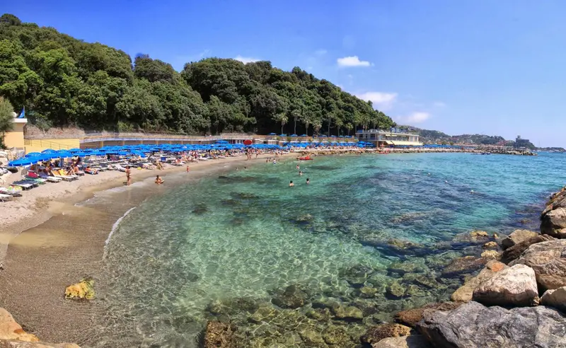 Une plage de galets bordée d'eau turquoise et de parasols colorés.