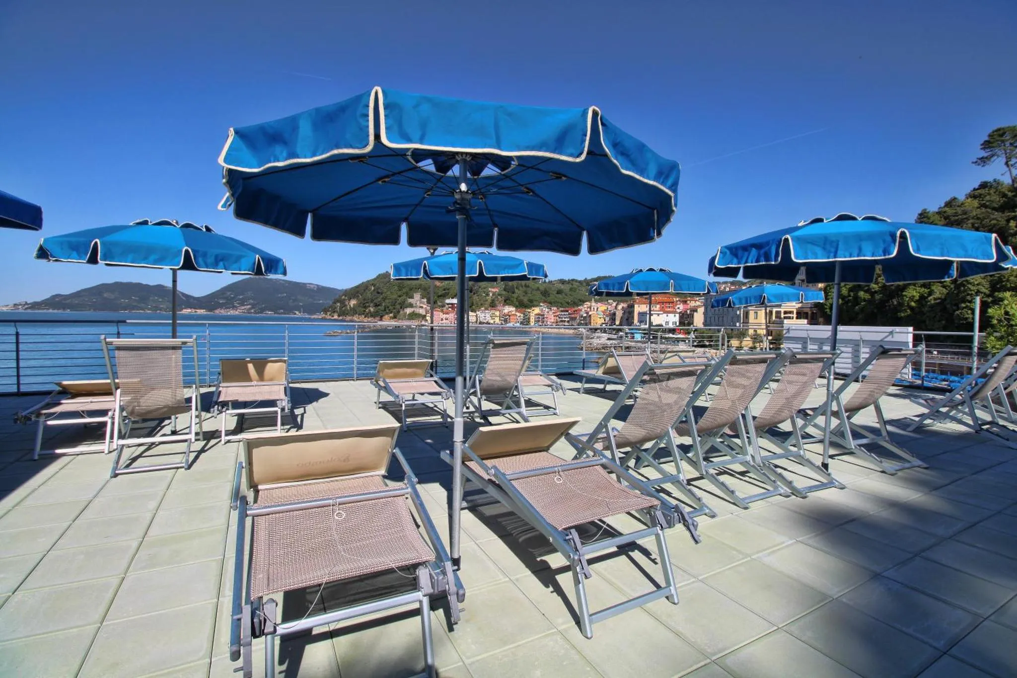 Terrasse ensoleillée avec transats bleus et vue sur la mer.