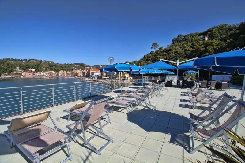 Terrasse ensoleillée avec transats bleus et vue sur la mer.