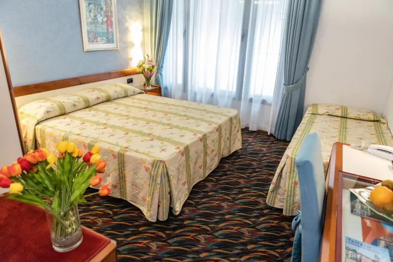 Une chambre d'hôtel avec deux lits et un bouquet de fleurs sur une table de chevet.