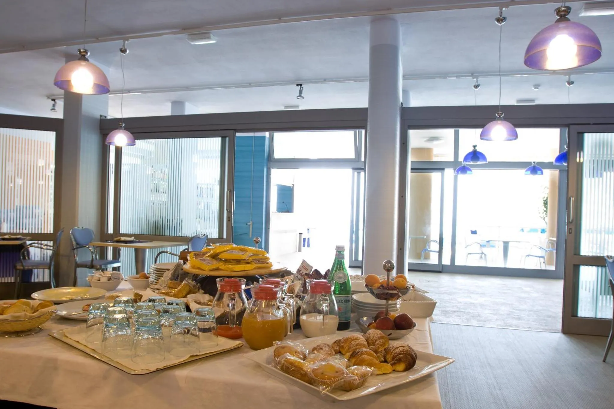 Un buffet propose des viennoiseries, des fruits et des boissons dans une salle lumineuse.