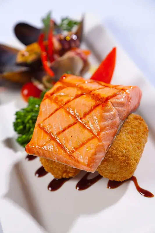 Un plat de poisson grillé est présenté avec des légumes et une sauce.