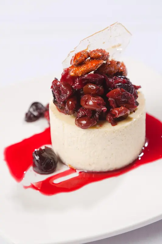 Un dessert crémeux est garni de fruits rouges et d'amandes effilées, servi avec une sauce rouge.