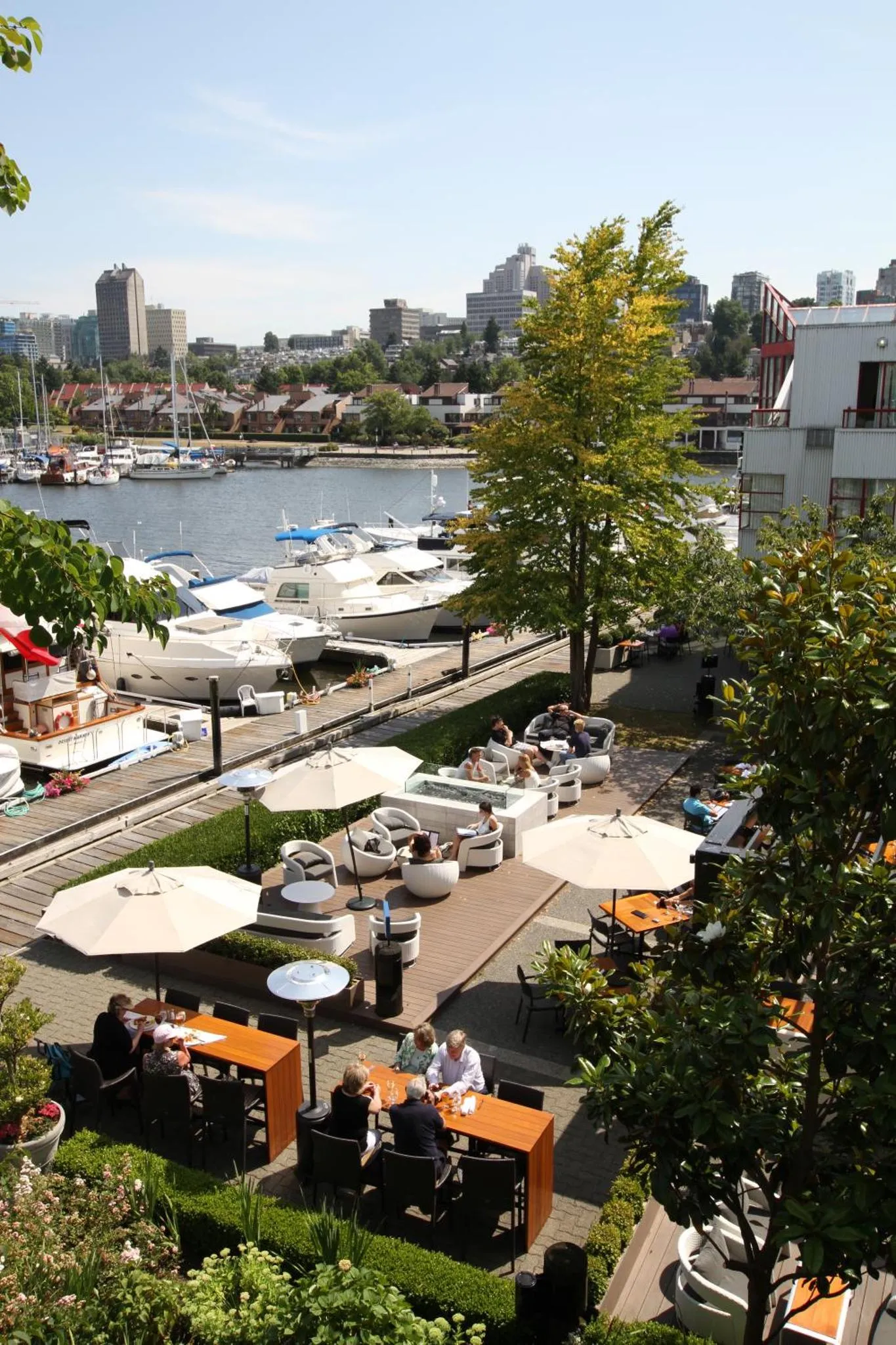Terrasse ombragée avec tables et chaises donnant sur un port de plaisance.
