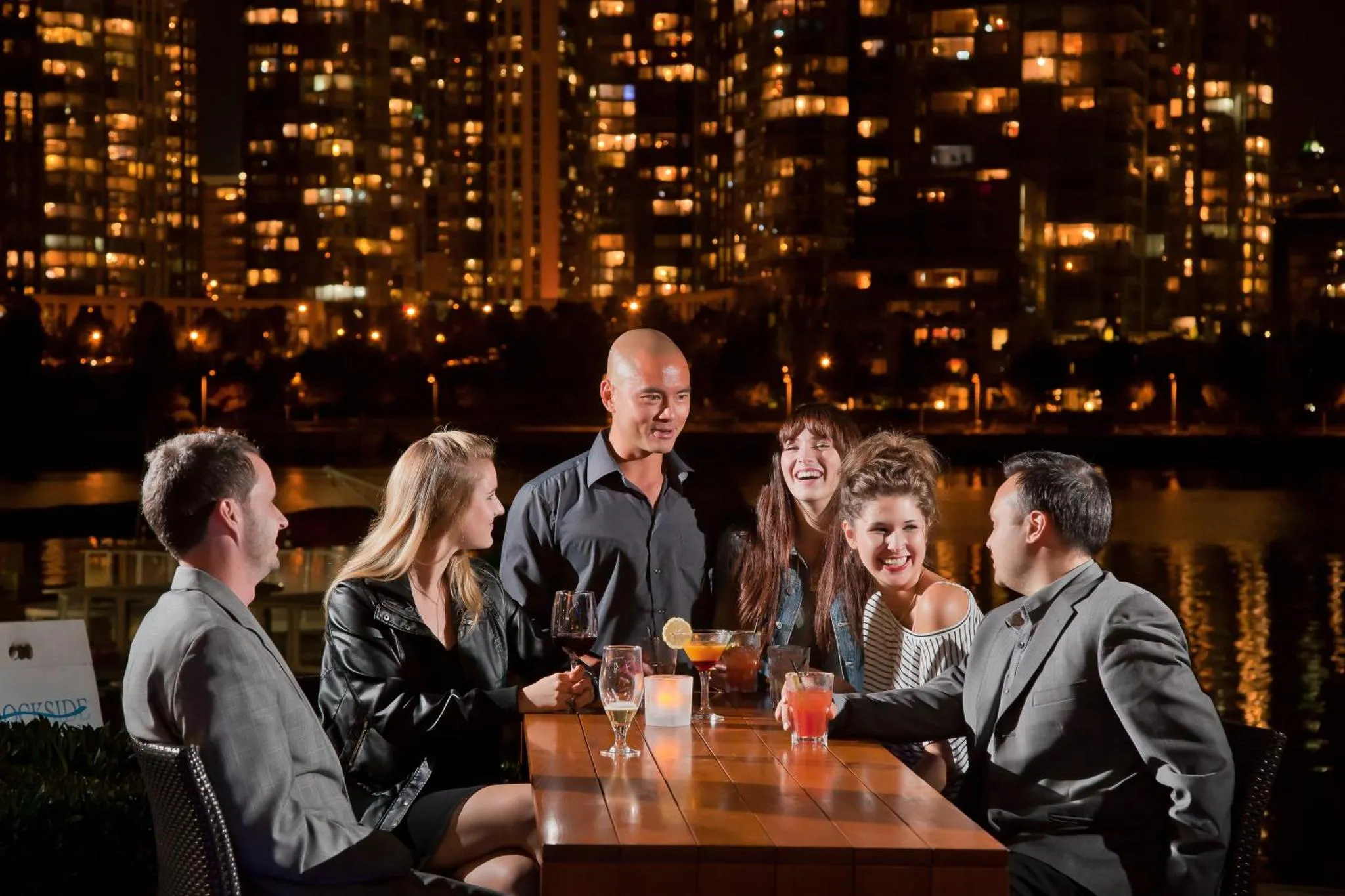Un groupe de personnes est assis autour d'une table en extérieur, avec une vue sur une ville illuminée.