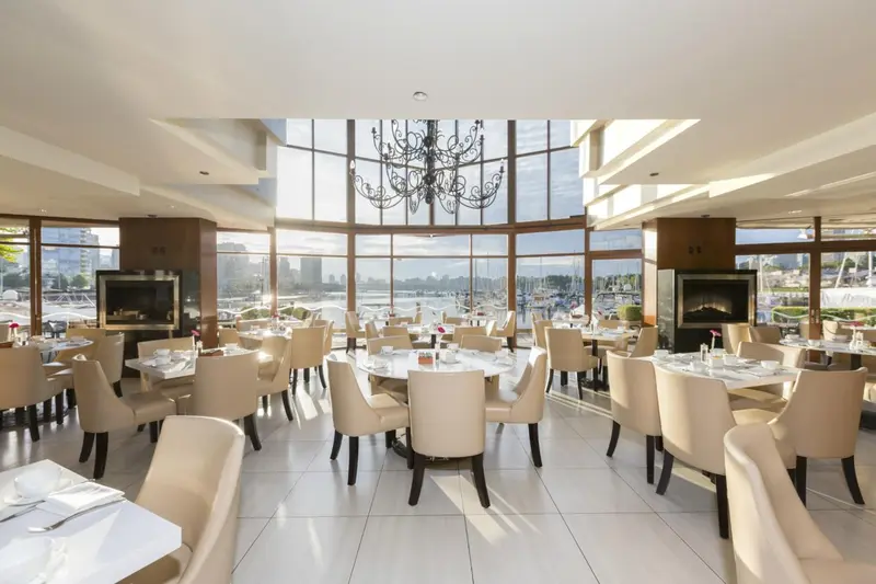 Une salle lumineuse avec des tables dressées face à une grande baie vitrée.