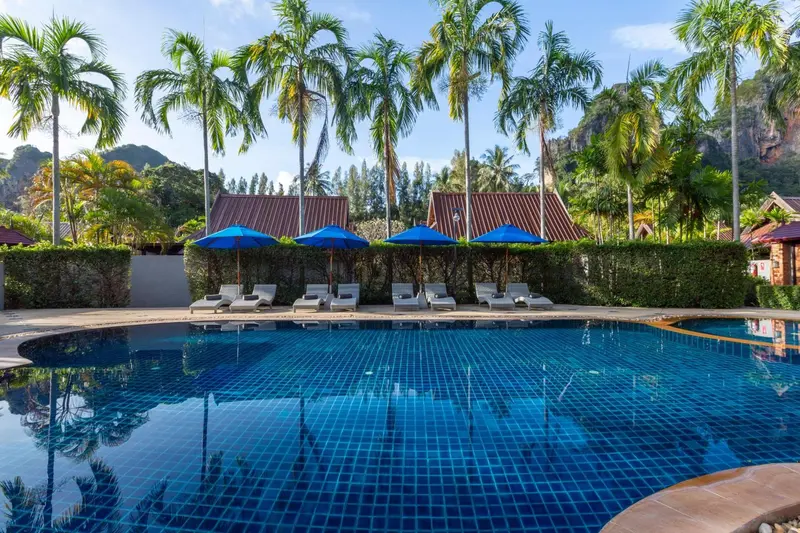 Transats alignés au bord d'une piscine turquoise entourée de végétation tropicale.