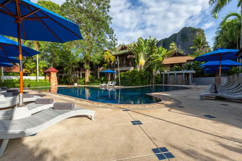 Une piscine rectangulaire bordée de chaises longues dans un jardin tropical.