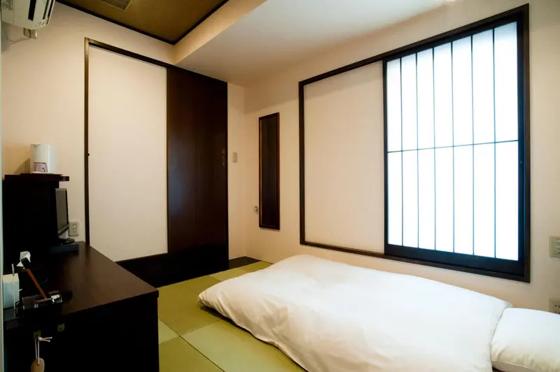 Une chambre minimaliste avec un lit sur tatami et une fenêtre à claustra.
