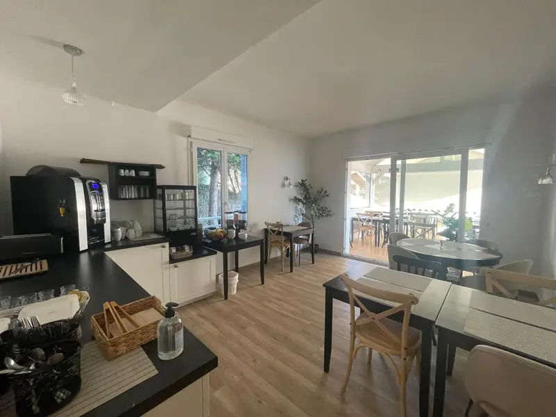 Une salle lumineuse avec un comptoir noir et des tables à manger en bois.