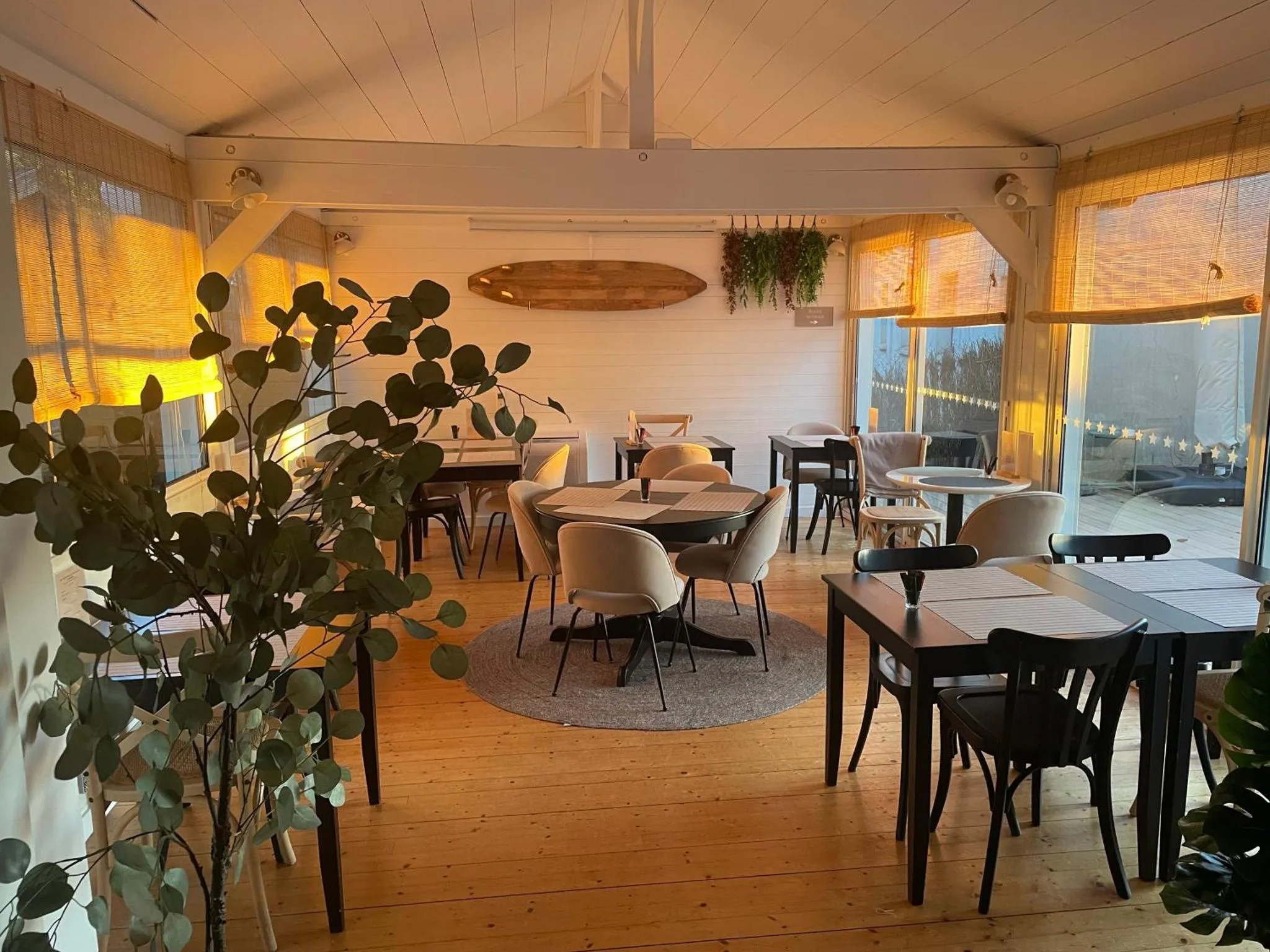 Une salle lumineuse avec des tables et des chaises est décorée de plantes et de rideaux.