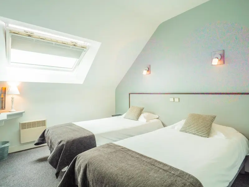 Une chambre mansardée avec deux lits simples et une décoration sobre.