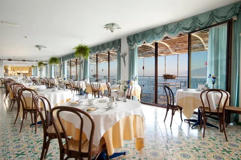 Une salle lumineuse avec des tables dressées face à une vue sur la mer.