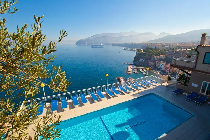 Vue aérienne sur une piscine d'hôtel avec transats et la mer en toile de fond.