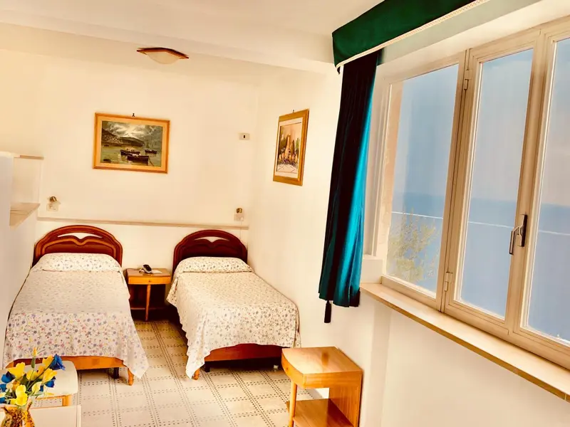Chambre lumineuse avec deux lits simples et vue sur la mer.