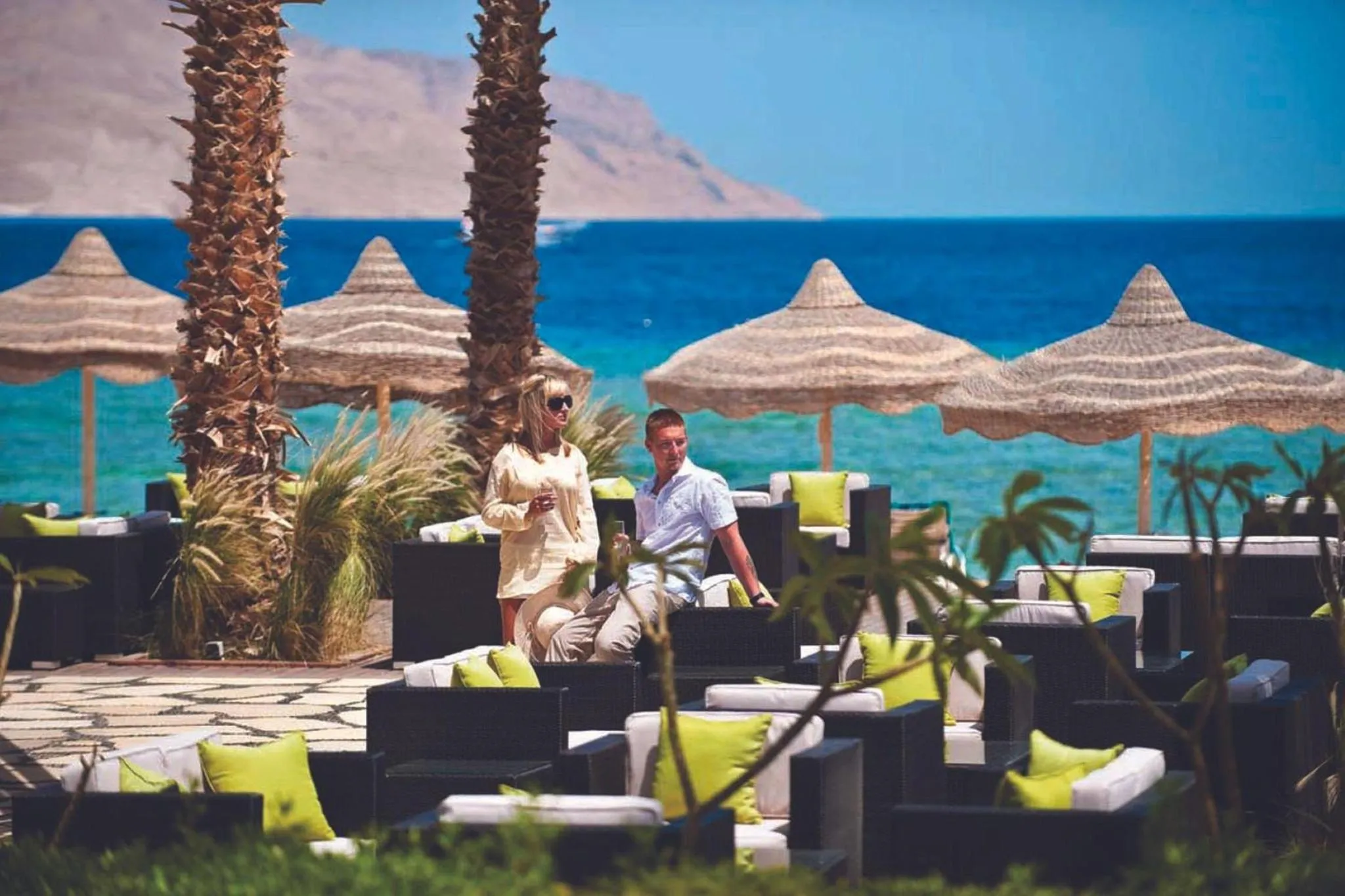 Deux personnes se détendent sur des canapés sous des parasols en bord de mer.