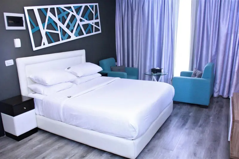 Une chambre lumineuse avec un grand lit blanc et deux fauteuils turquoise.
